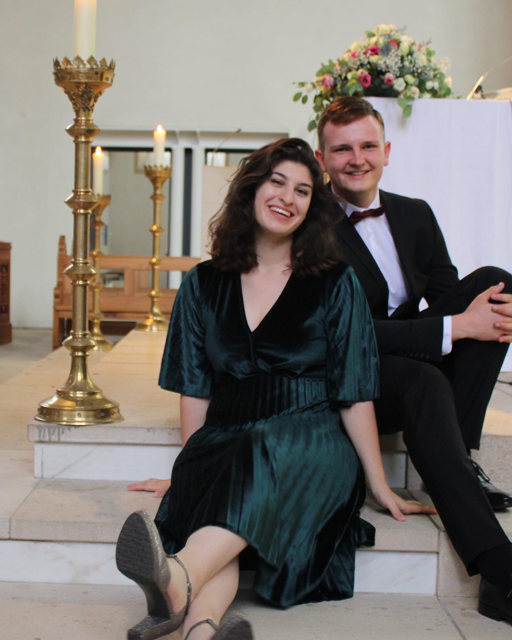 Dominik im Anzug und Sophia im grünen Kleid sitzen auf den Altarstufen einer Kirche