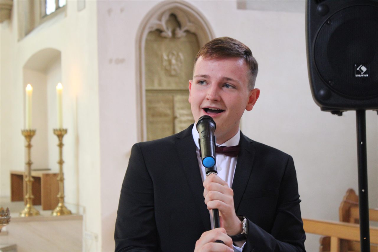 Dominik singt im Anzug mit Mikrofon vor dem Altarraum