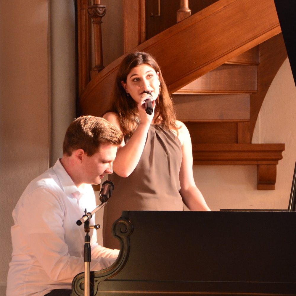 Sophia singt am Mikrofon, während Dominik sie am Flügel begleitet